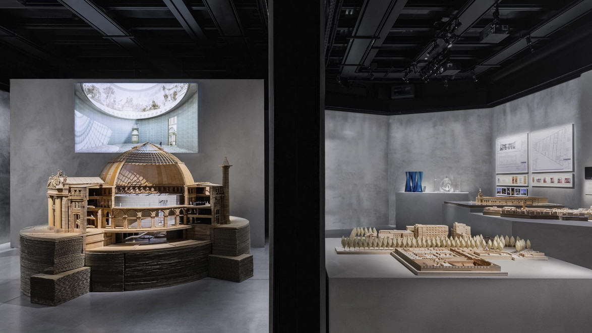 Exhibit room showcasing detailed architectural models and design sketches under soft lighting.