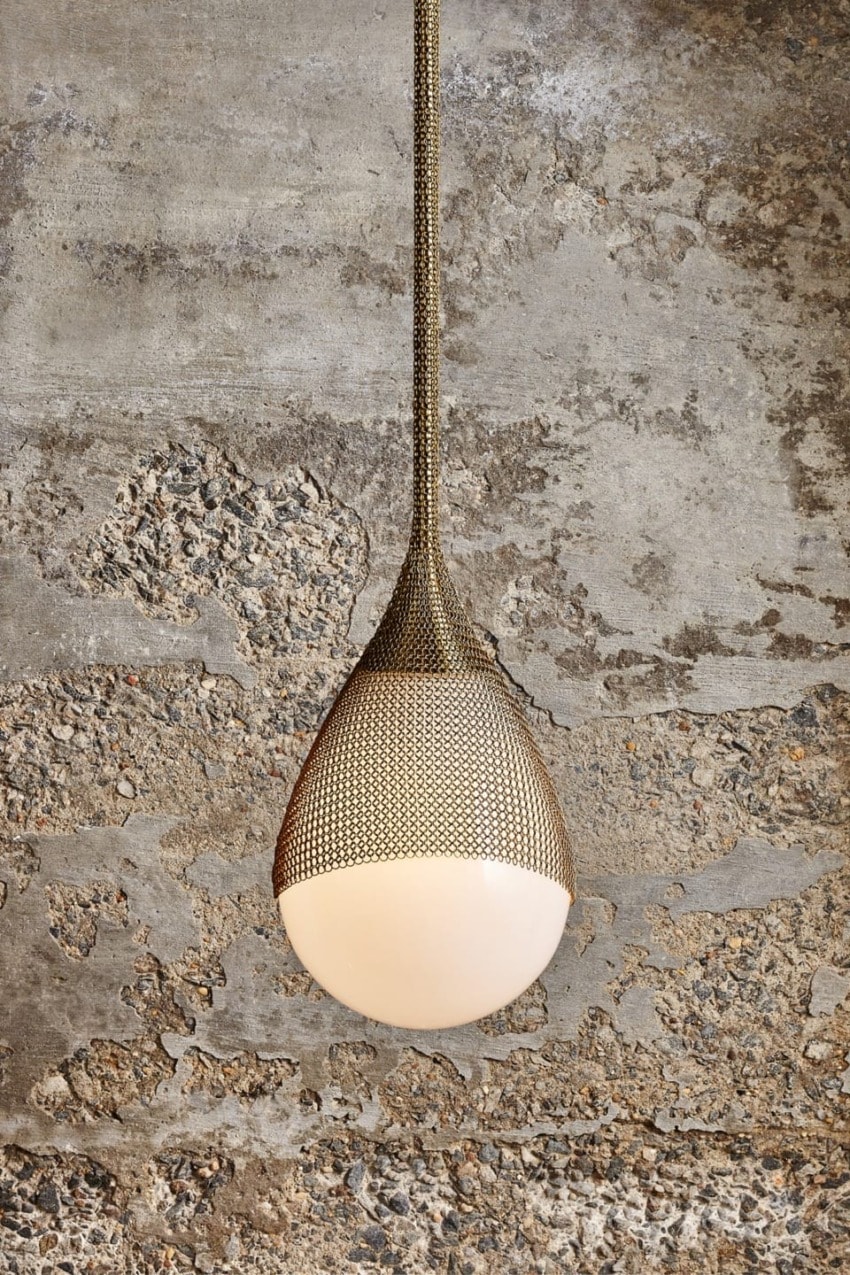 Modern pendant light with a mesh-like texture hanging against a textured concrete wall background.