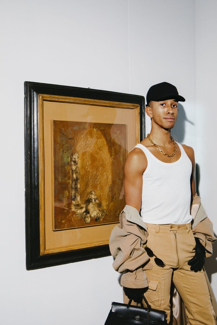 Person in a white tank top and cap standing by an abstract painting in a gallery setting.