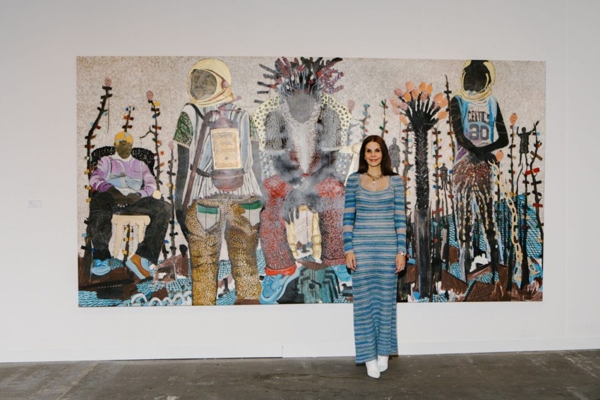Person standing in front of a large colorful painting featuring four abstract figures in an art gallery setting.