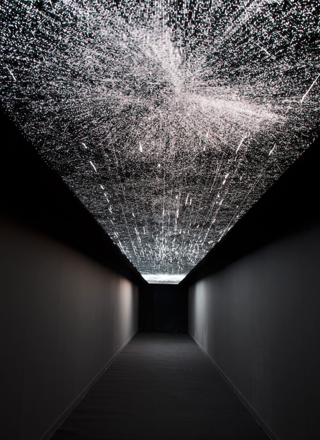 Art installation with glowing, starry light pattern on a ceiling in a dimly lit corridor.