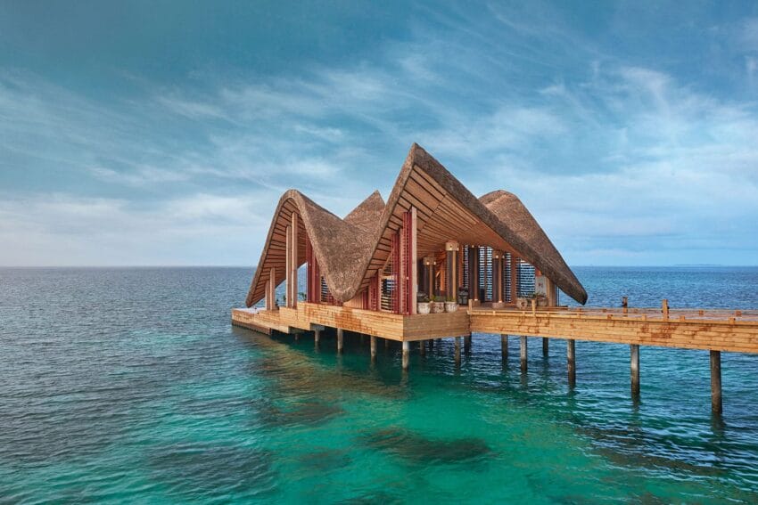 Wooden pier building with unique triangular roofs overlooking clear blue ocean and sky.