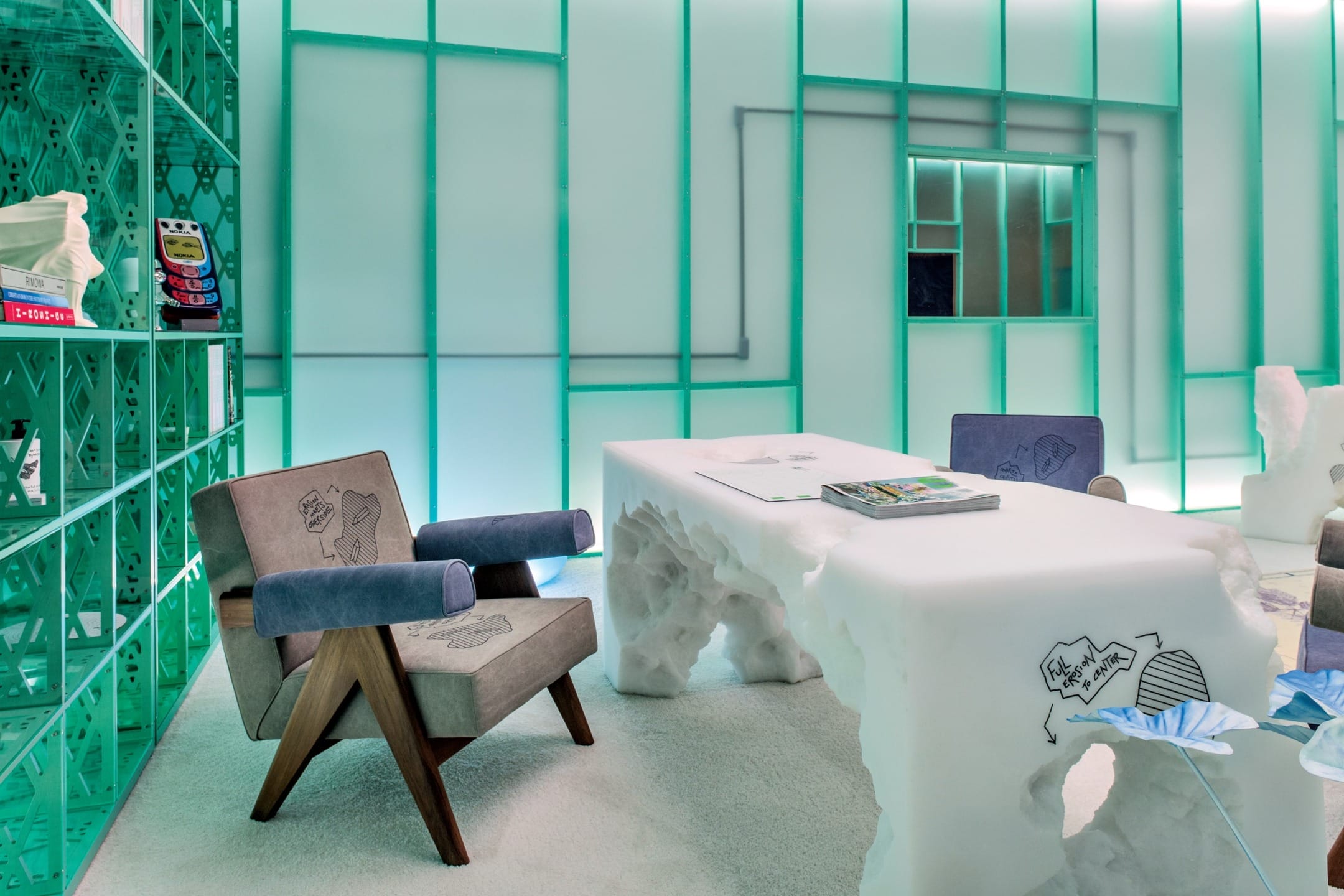 Futuristic office with a carved desk, modern chairs, and glowing teal shelving against a sleek, illuminated wall.