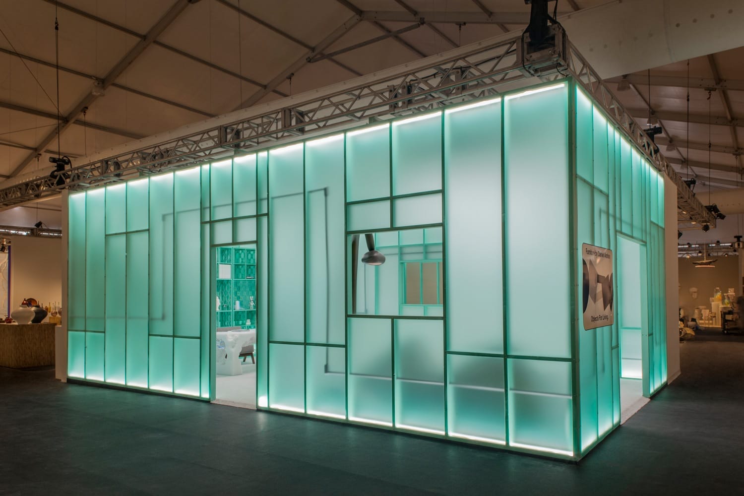 Modern exhibition booth with glowing turquoise panels and geometric design under a large tent.