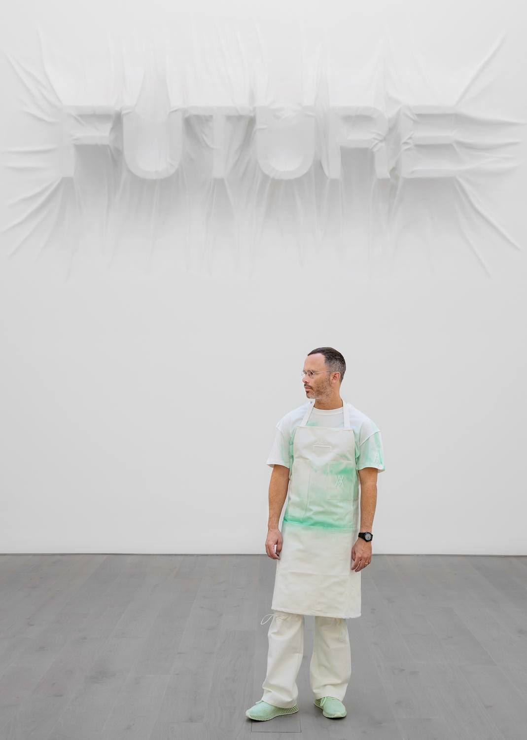 Man standing in a gallery with the word "FUTURE" sculpted on the wall behind him.