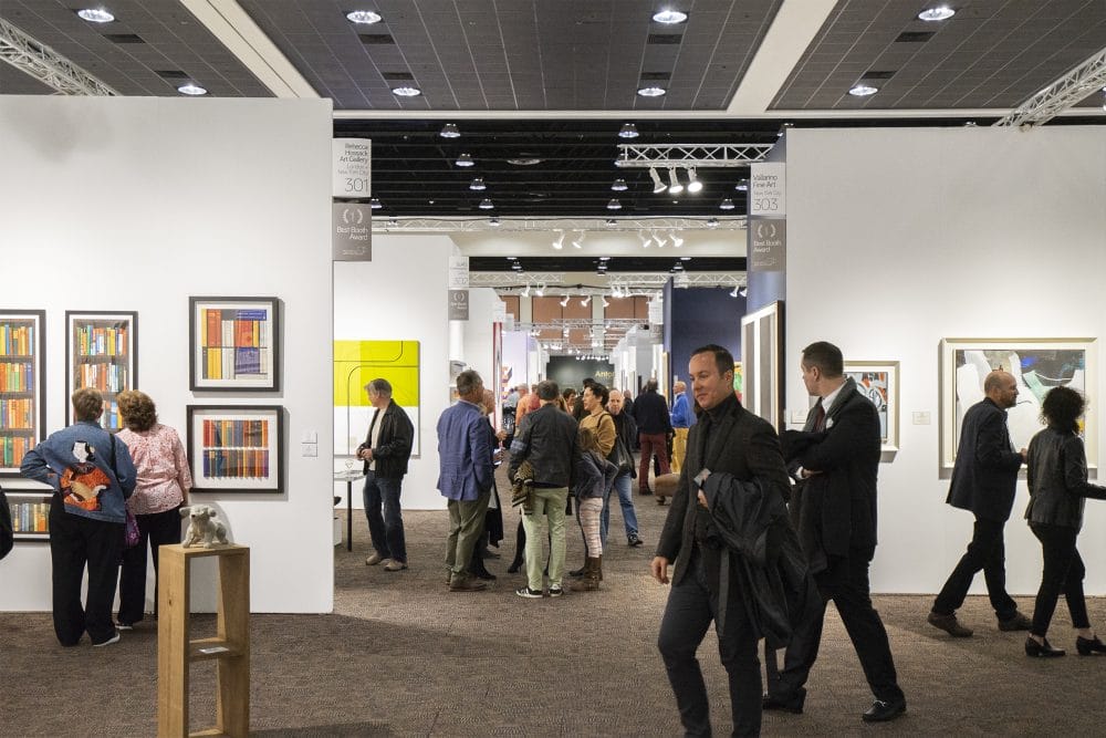 People exploring a modern art gallery with colorful paintings displayed on white walls and sculptures on pedestals.