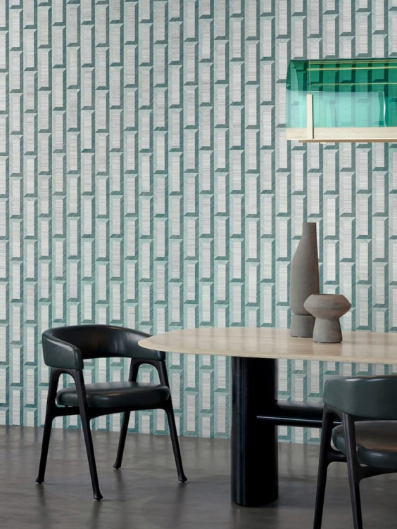 Modern dining area with geometric wallpaper, green chairs, a wooden table, decorative vases, and a unique glass light fixture.