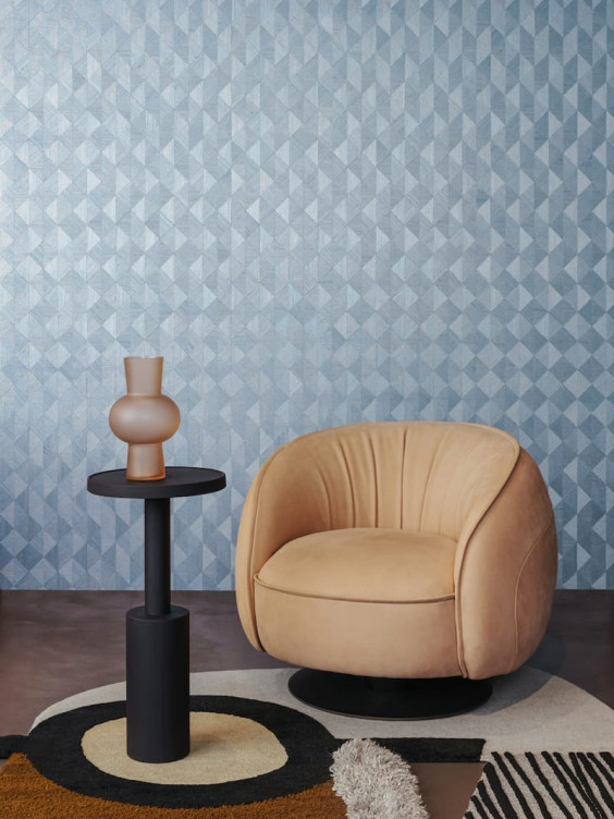 Modern living room with a beige armchair, geometric patterned wallpaper, and a black accent table with a vase.