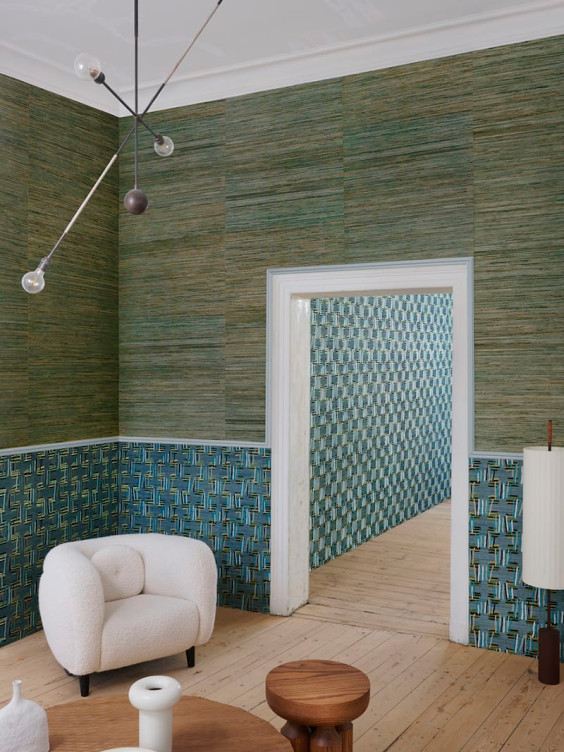 Modern interior with green textured walls, geometric patterns, and minimalist furniture, including a white armchair and round table.