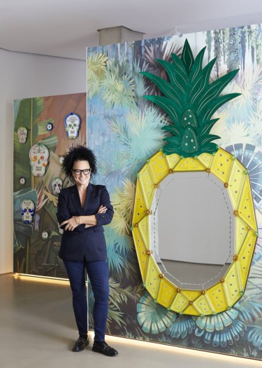 Person standing beside a pineapple-shaped mirror with colorful mural background featuring skull art.