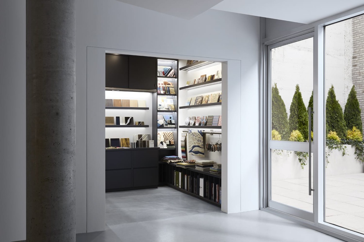 Modern library space with sleek shelves displaying books and magazines next to large glass doors leading to outdoor greenery.