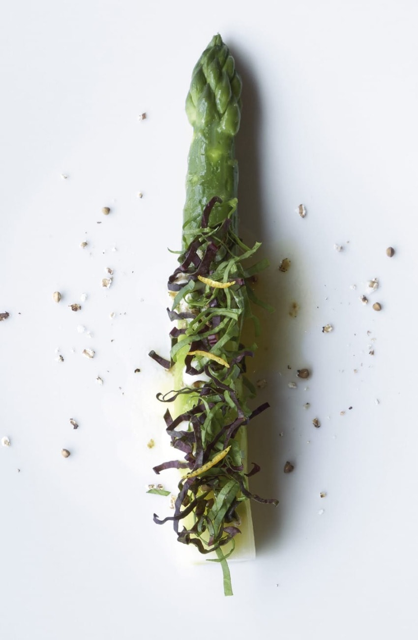 Asparagus spear garnished with shredded greens and cracked pepper on a white background.