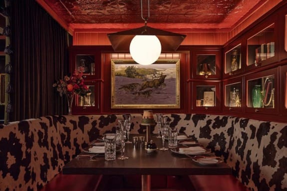 Cozy restaurant dining area with cow-print seating, elegant table setting, pendant light, and artwork on paneled walls.