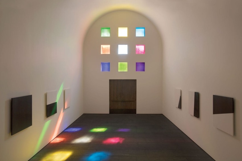 Modern art gallery with colorful square windows casting light patterns on the floor and abstract paintings on the walls.