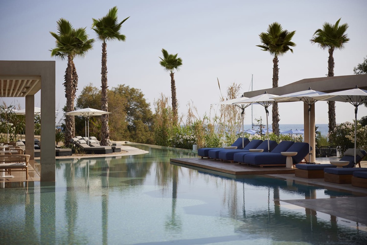 Luxury resort pool with sun loungers, umbrellas, and palm trees under a clear sky.