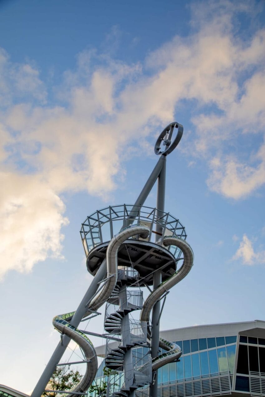 Tall twisting outdoor slide with observation deck against a blue sky and clouds at an amusement or adventure park