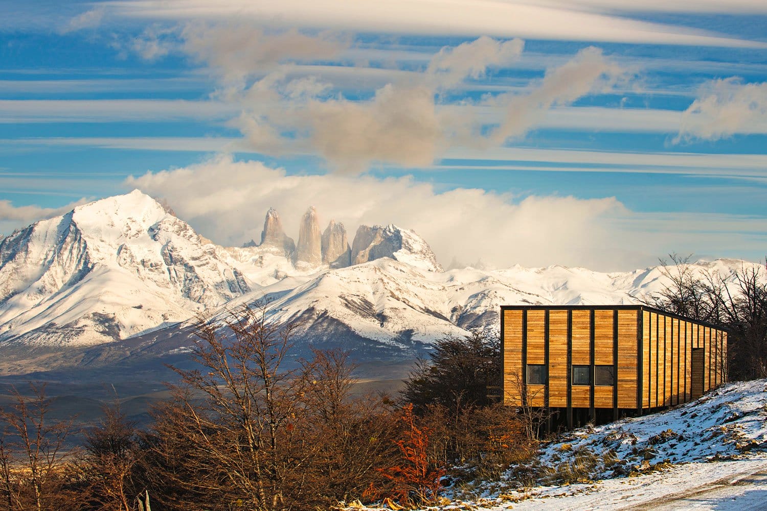 Wooden cabin with snowy mountains and cloudy sky in the background at Torres del Paine National Park, Chile.