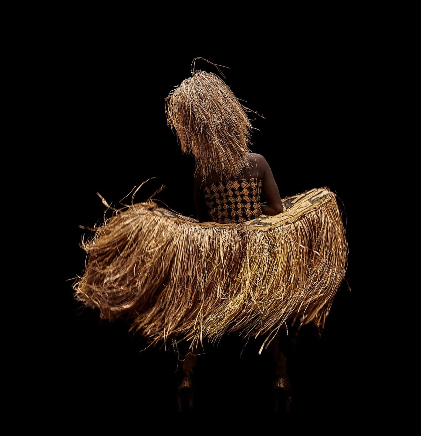 Dancer wearing traditional costume made of woven straw against a black background.