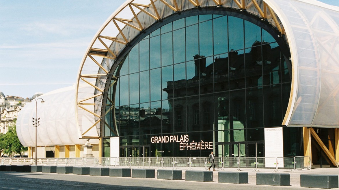 Exterior view of Grand Palais Éphémère with large glass facade and wooden arches under a clear blue sky.