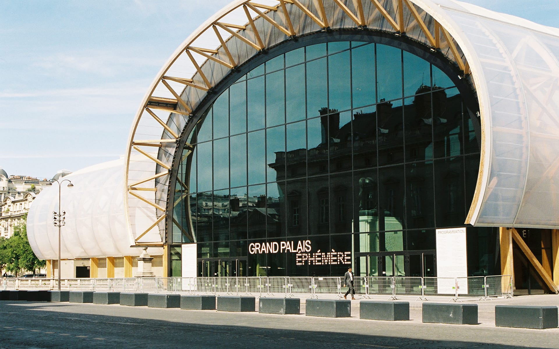 Exterior view of Grand Palais Éphémère with large glass facade and wooden arches under a clear blue sky.