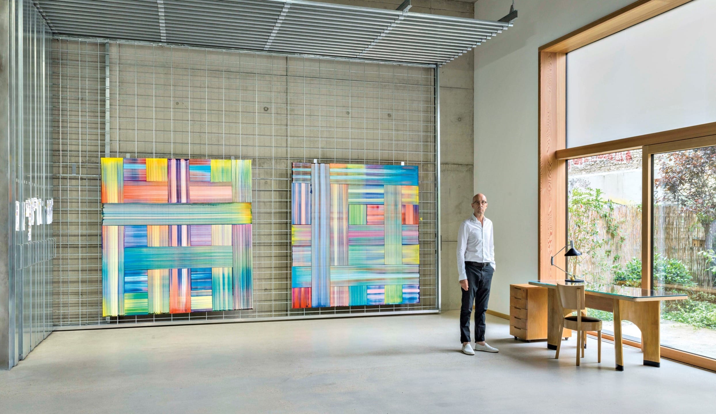 Man standing in a modern art gallery with colorful abstract paintings on display, large window to the right.