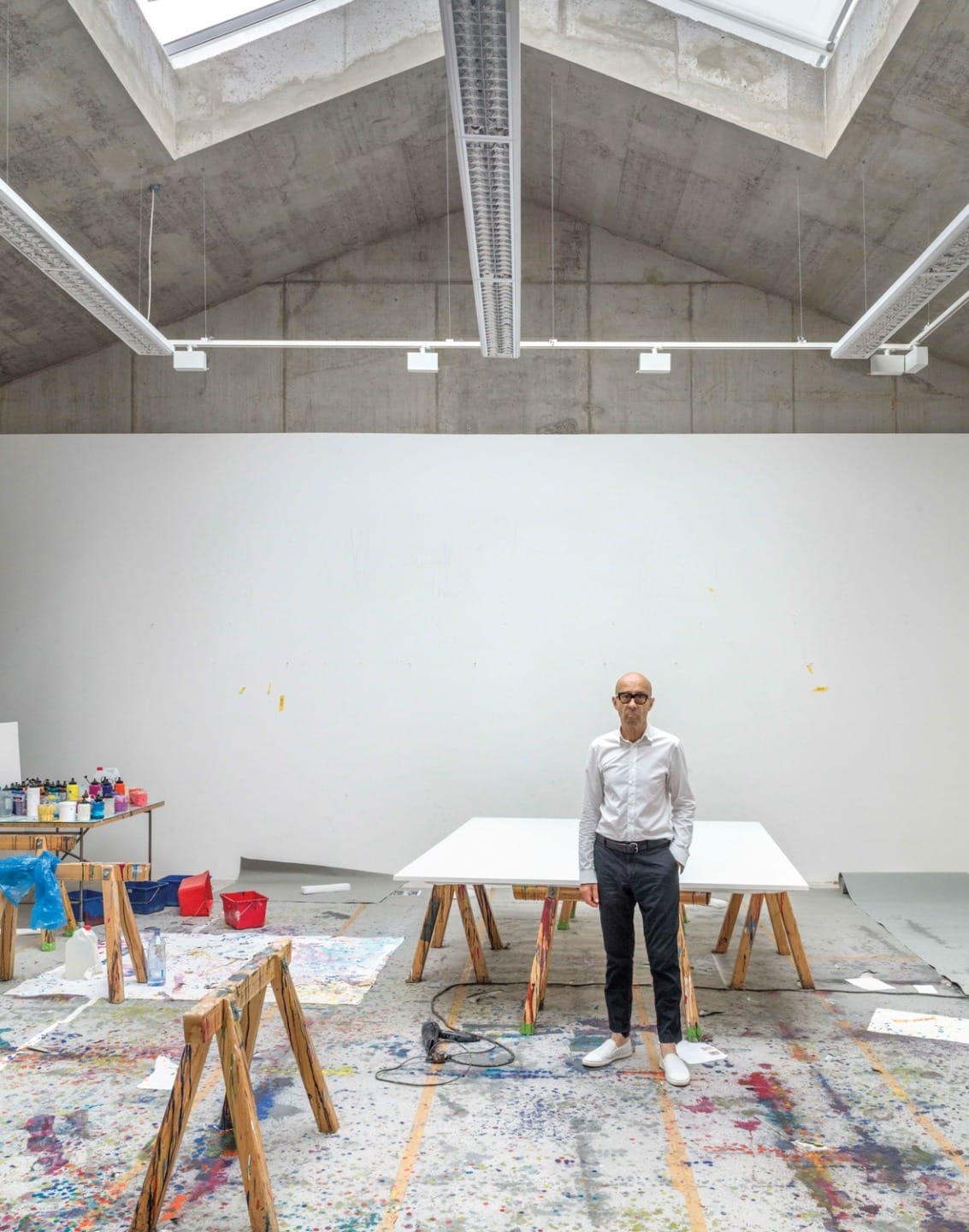 Artist standing in a spacious, light-filled studio with canvases and art supplies on the floor.