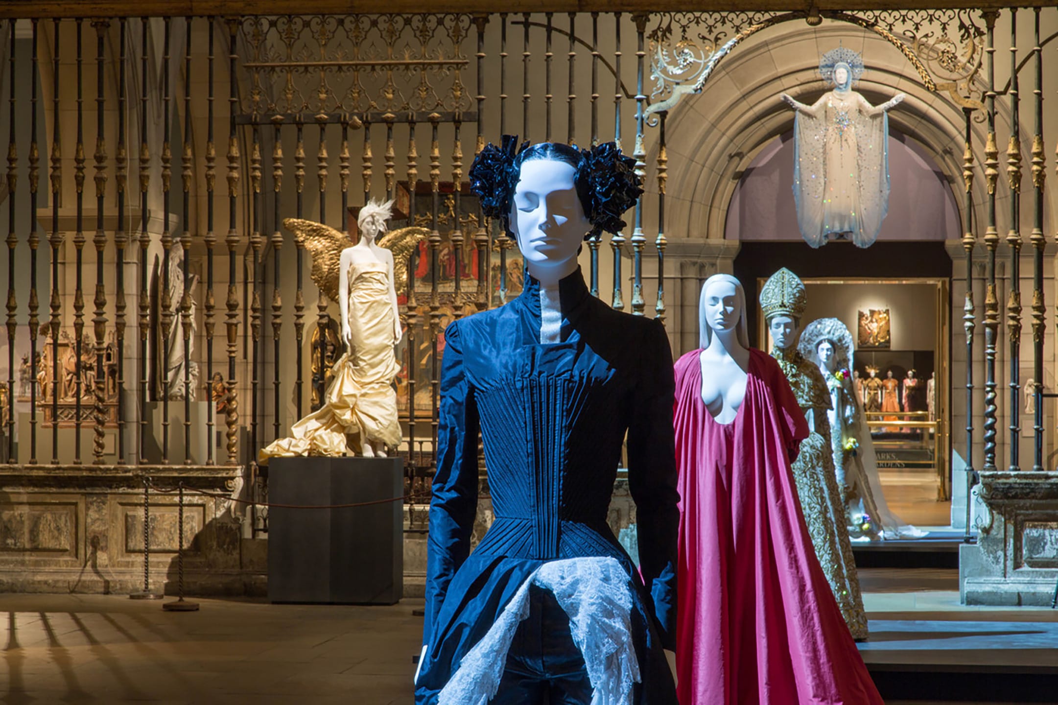 Exhibit of mannequins in ornate dresses displayed in a historical museum setting with sculptures and decorative elements.
