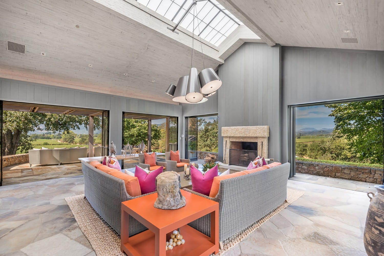 Modern living room with large windows, stylish seating, colorful pillows, and a view of the outdoors.