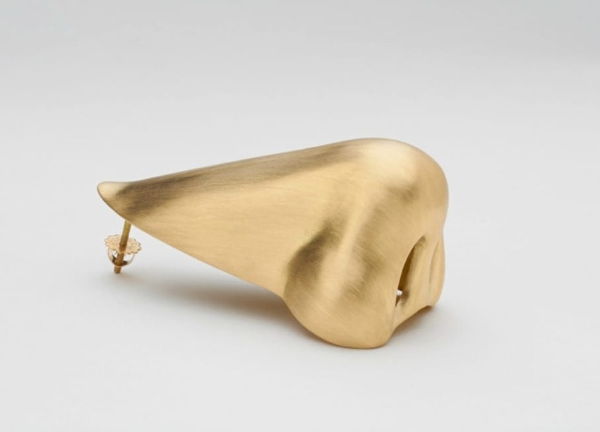 Gold sculpted nose-shaped earring on a white background.