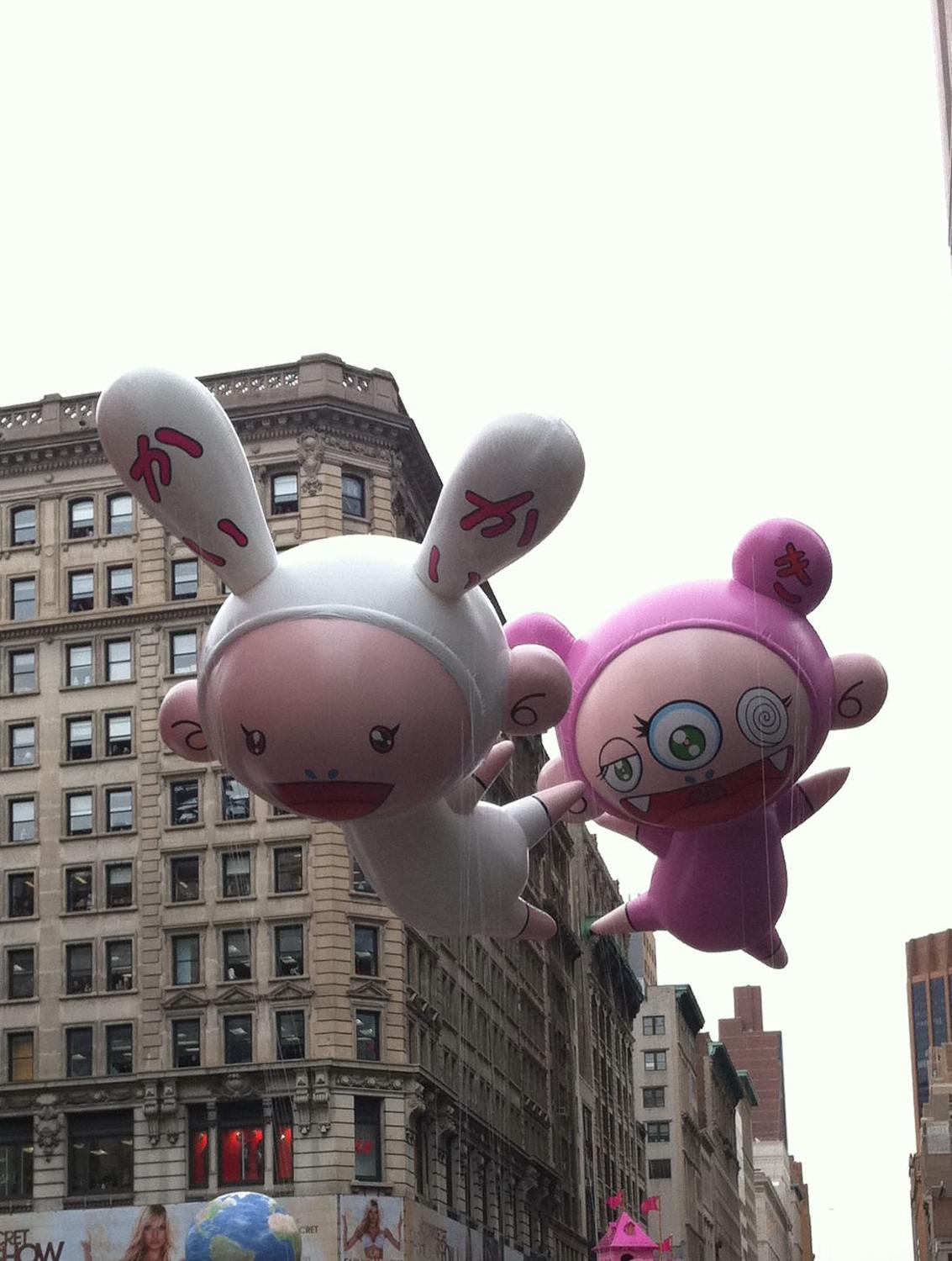 Giant inflatable characters floating in a city parade with tall buildings in the background