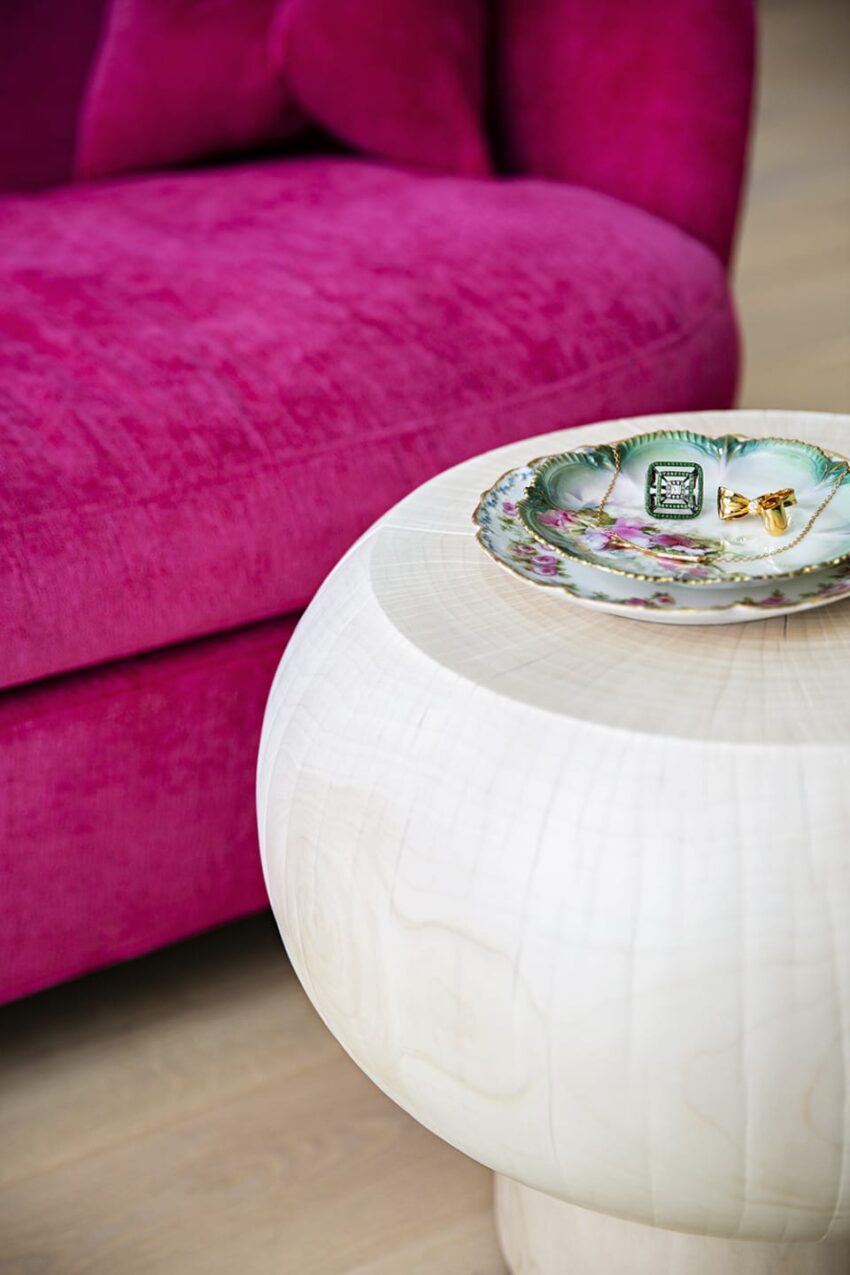 Modern white round table with decorative plate and jewelry, next to a vibrant pink sofa.