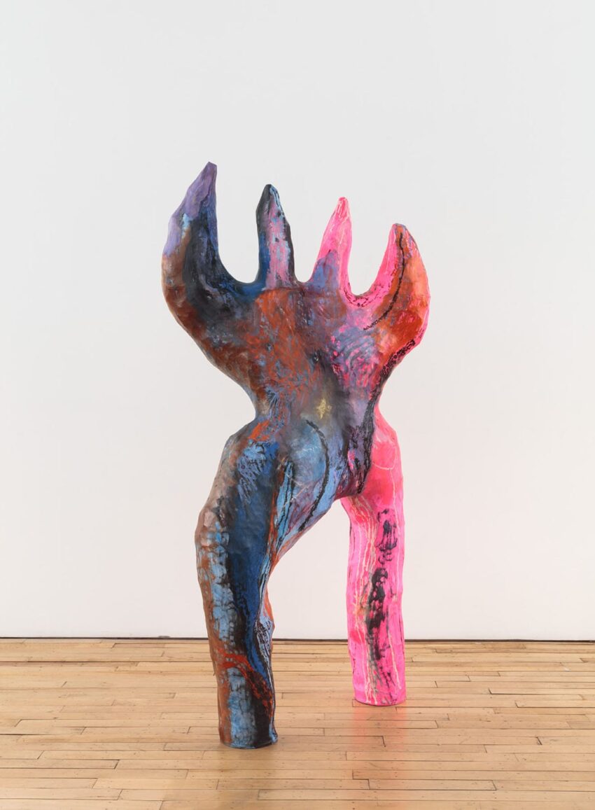 Colorful abstract sculpture with organic forms on a wooden floor against a white wall.