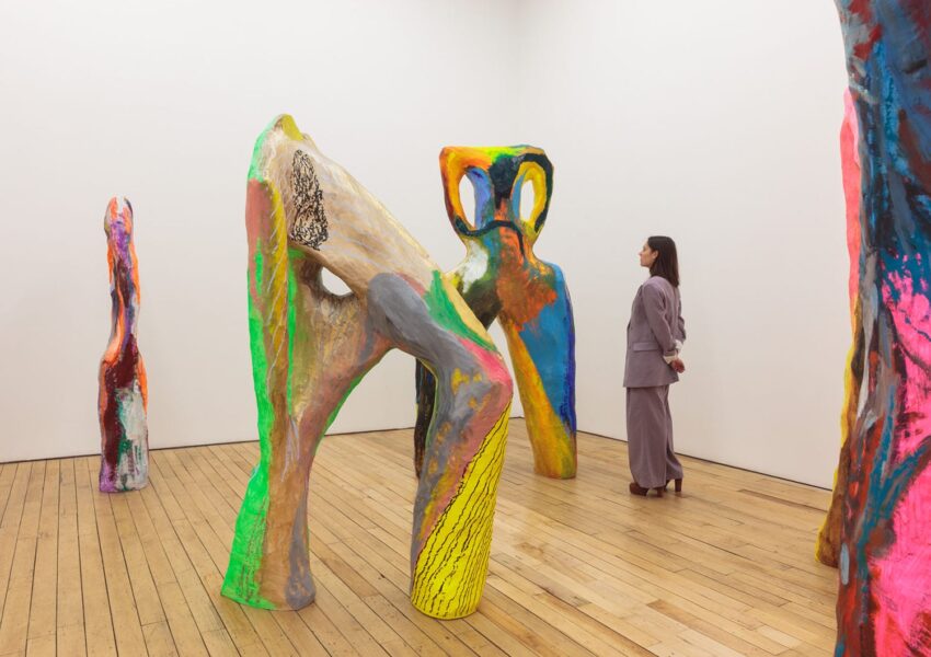 Woman observing colorful abstract sculptures in a gallery with wooden floors and white walls.