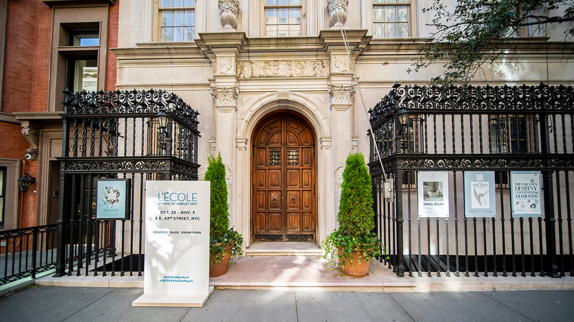 Entrance of a historic building with ornate iron gates and a large wooden door, located on a city street.