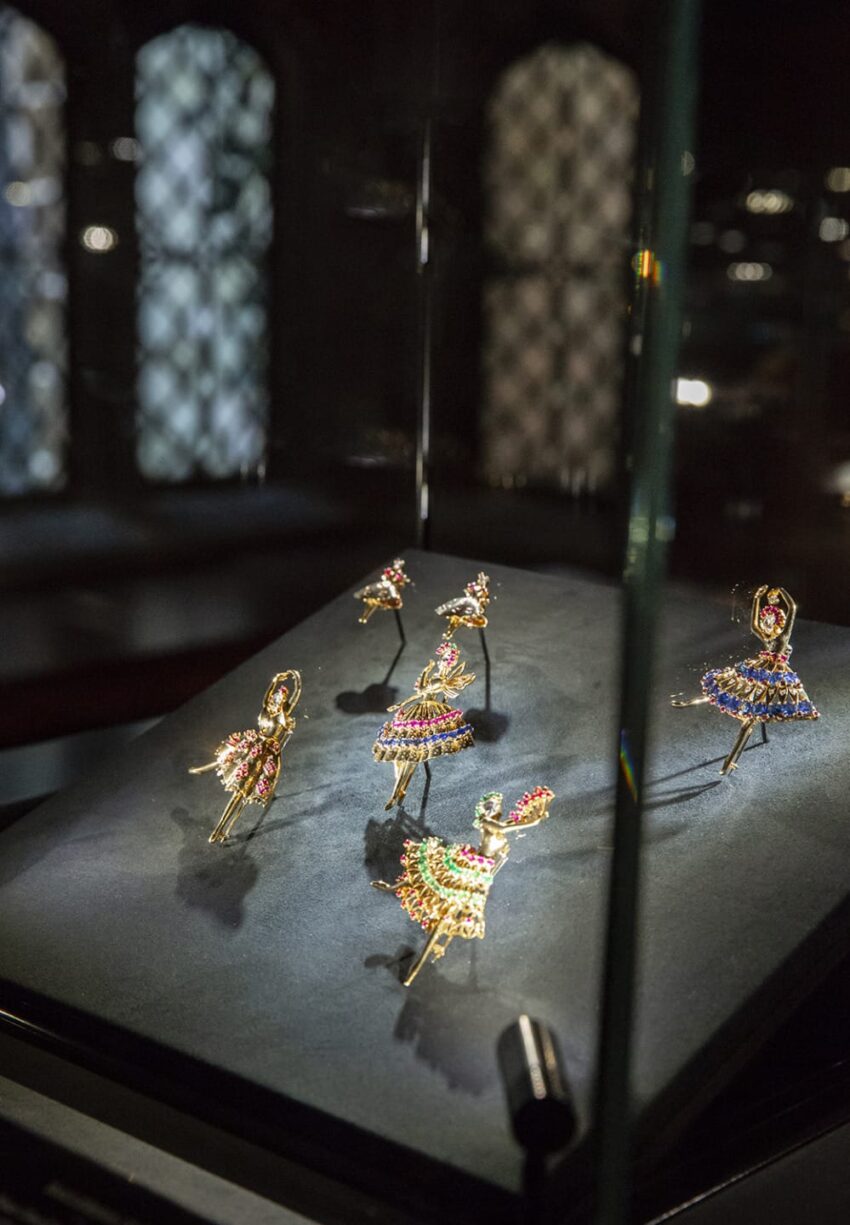 Ballet dancer brooches displayed in a dimly lit glass case, adorned with colorful jewels and intricate detailing.