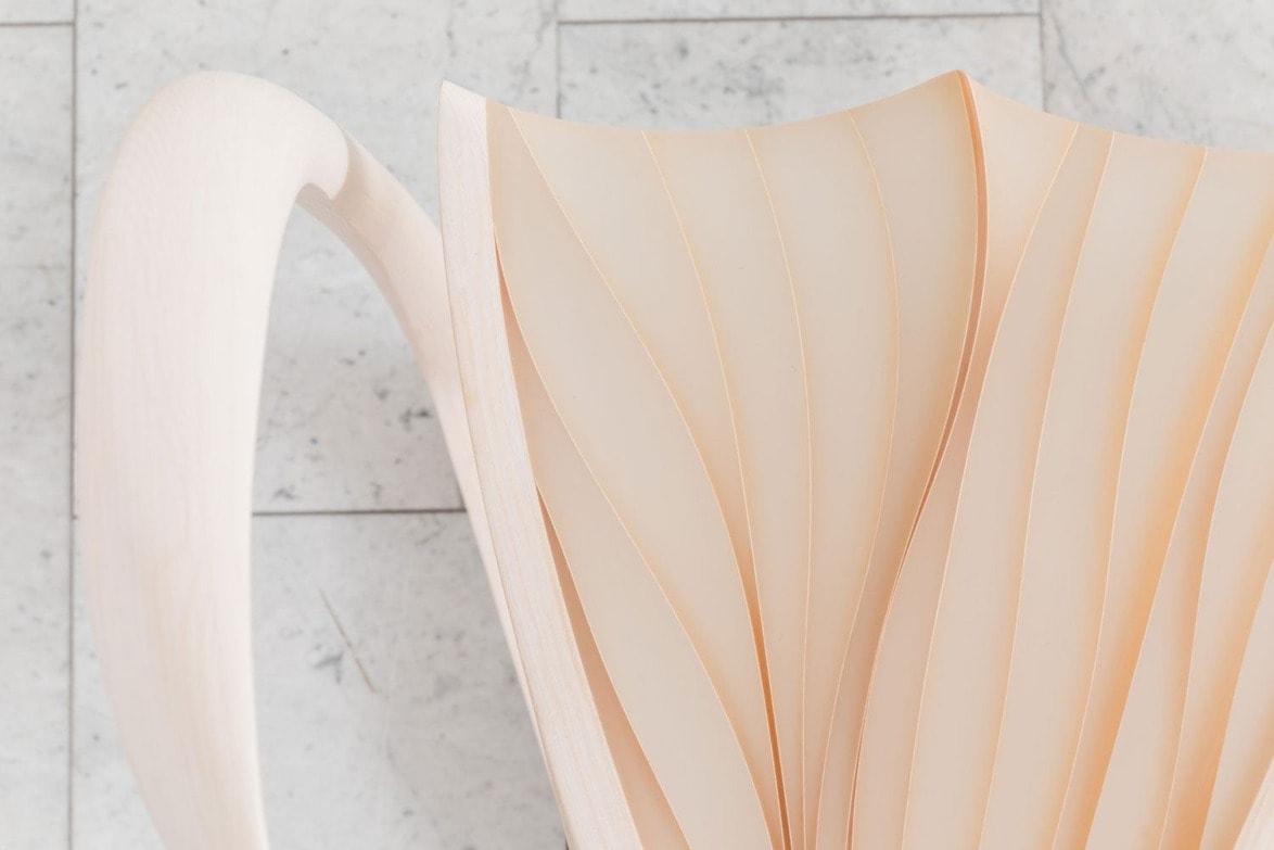 Elegant modern chair with a smooth white wood frame and curved seat design on a tiled floor background.