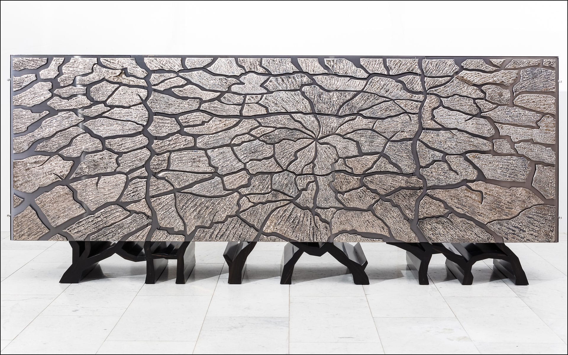 Abstract wooden sculpture resembling a cracked surface with a dark base, displayed in a gallery setting.