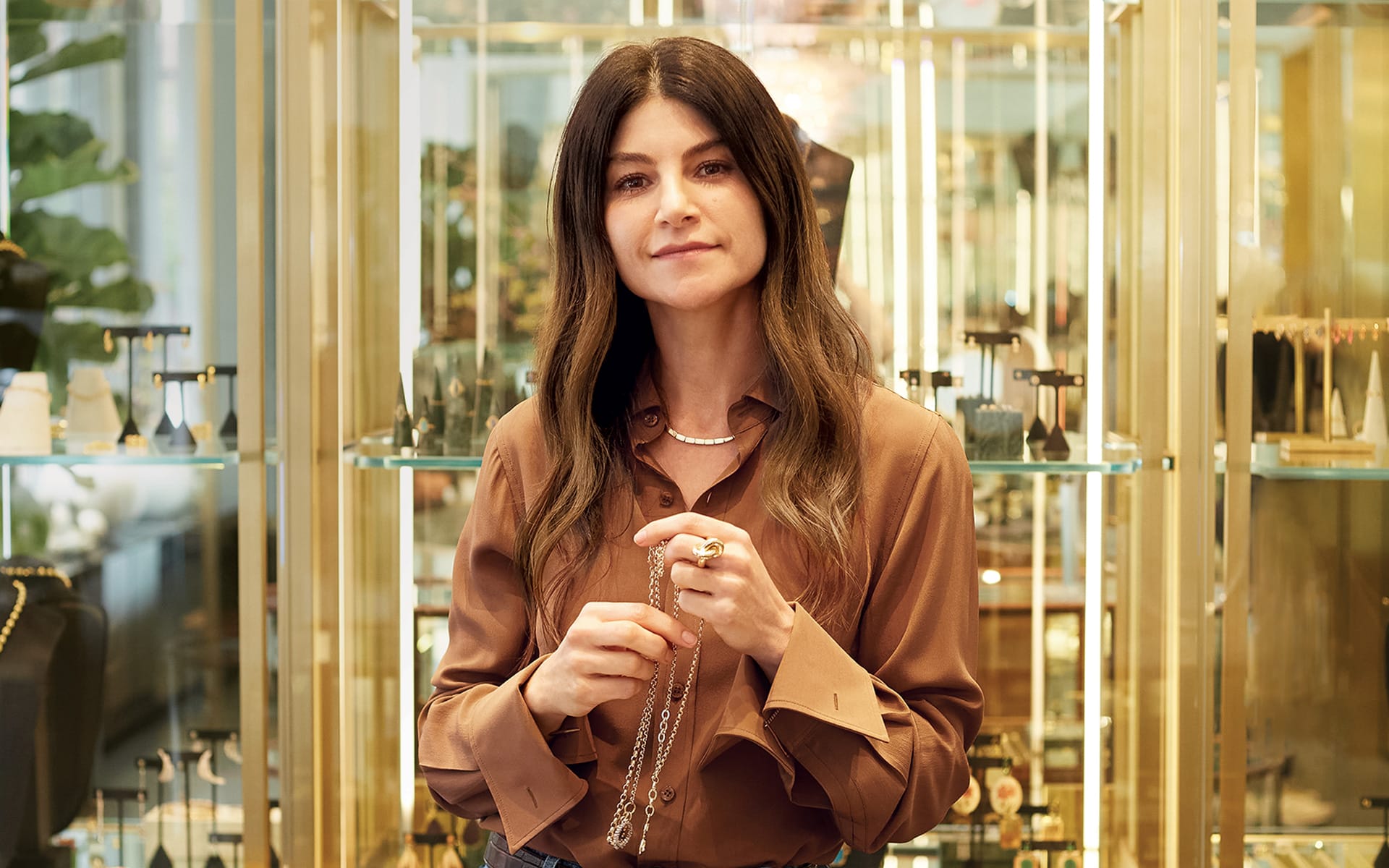 Person in brown shirt holding jewelry in front of display cases filled with various accessories and decor items.