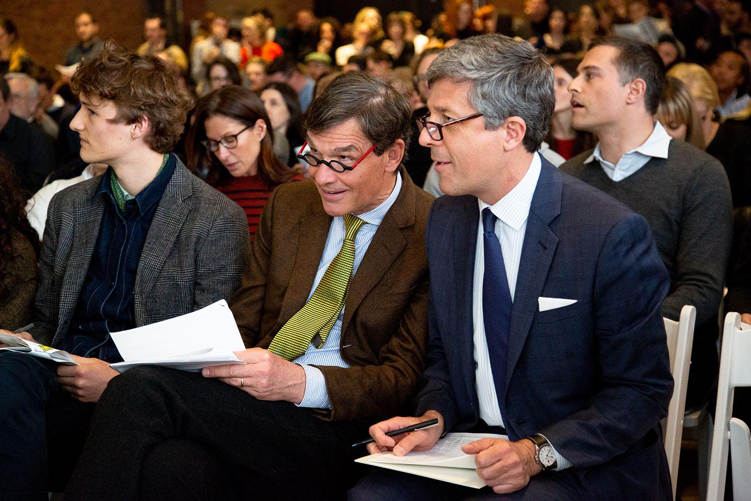Audience members engaged in a discussion during a conference or event, with a focus on two individuals seated in the foreground.