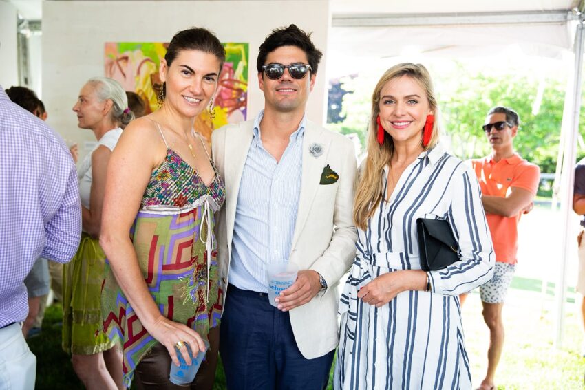 Group of three people smiling at an outdoor event in casual summer attire.