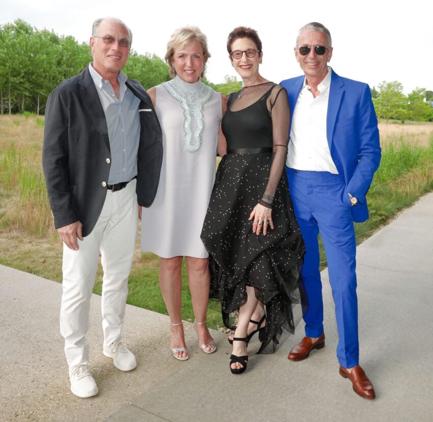 Four adults standing together outdoors, dressed in formal attire, smiling at the camera.