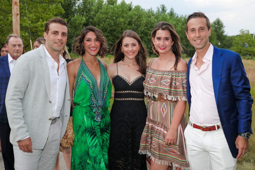 Group of five people smiling and posing outdoors at a gathering with trees in the background