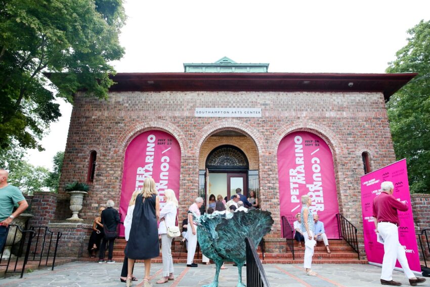 People gathered outside a brick building with pink banners for an event at the Southampton Arts Center.
