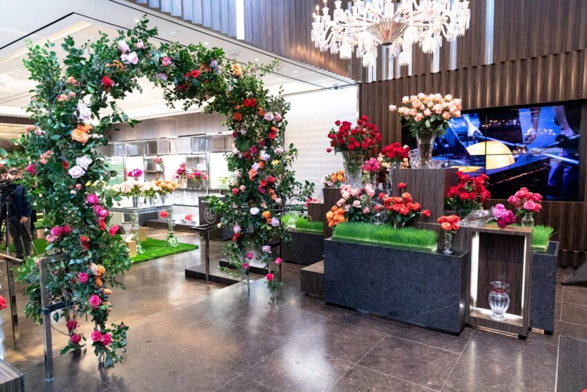 Elegant floral display with vibrant roses and greenery arranged under a chandelier in a modern interior setting.