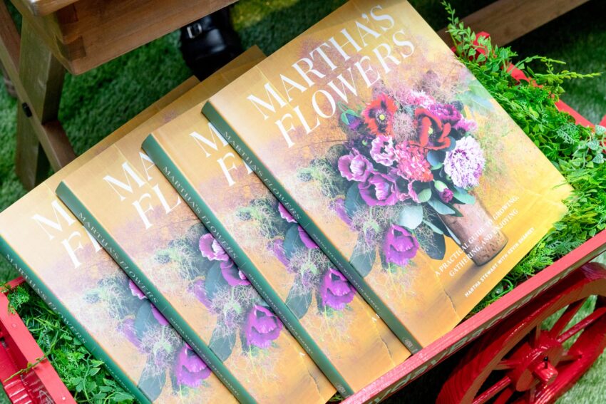 Four copies of Martha's Flowers book with a floral cover displayed on a bed of green leaves in a red wooden cart.