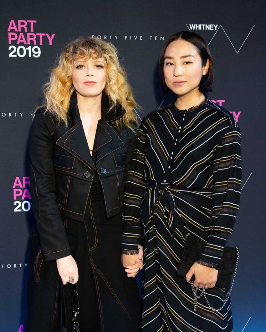 Two individuals holding hands at a 2019 art party event, standing in front of a branded backdrop.