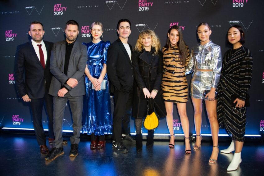 A group of eight stylishly dressed people posing at a 2019 art party event backdrop.