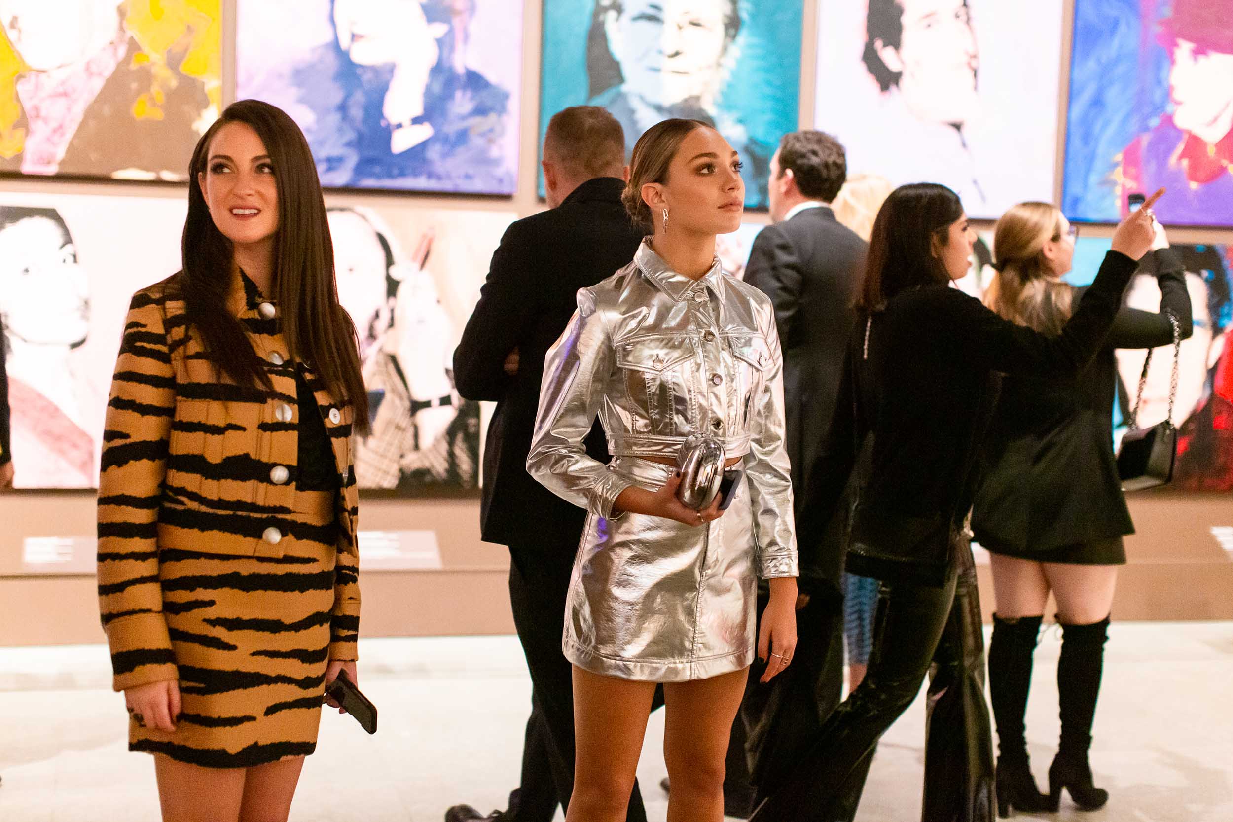 People viewing colorful pop art paintings in a gallery setting, with vibrant outfits and lively atmosphere.