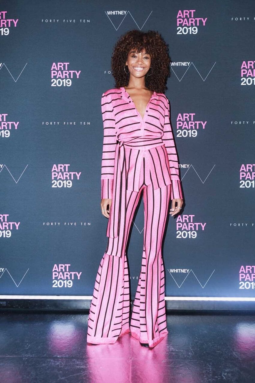 Person in pink and black striped outfit posing in front of a backdrop with "Art Party 2019" text.