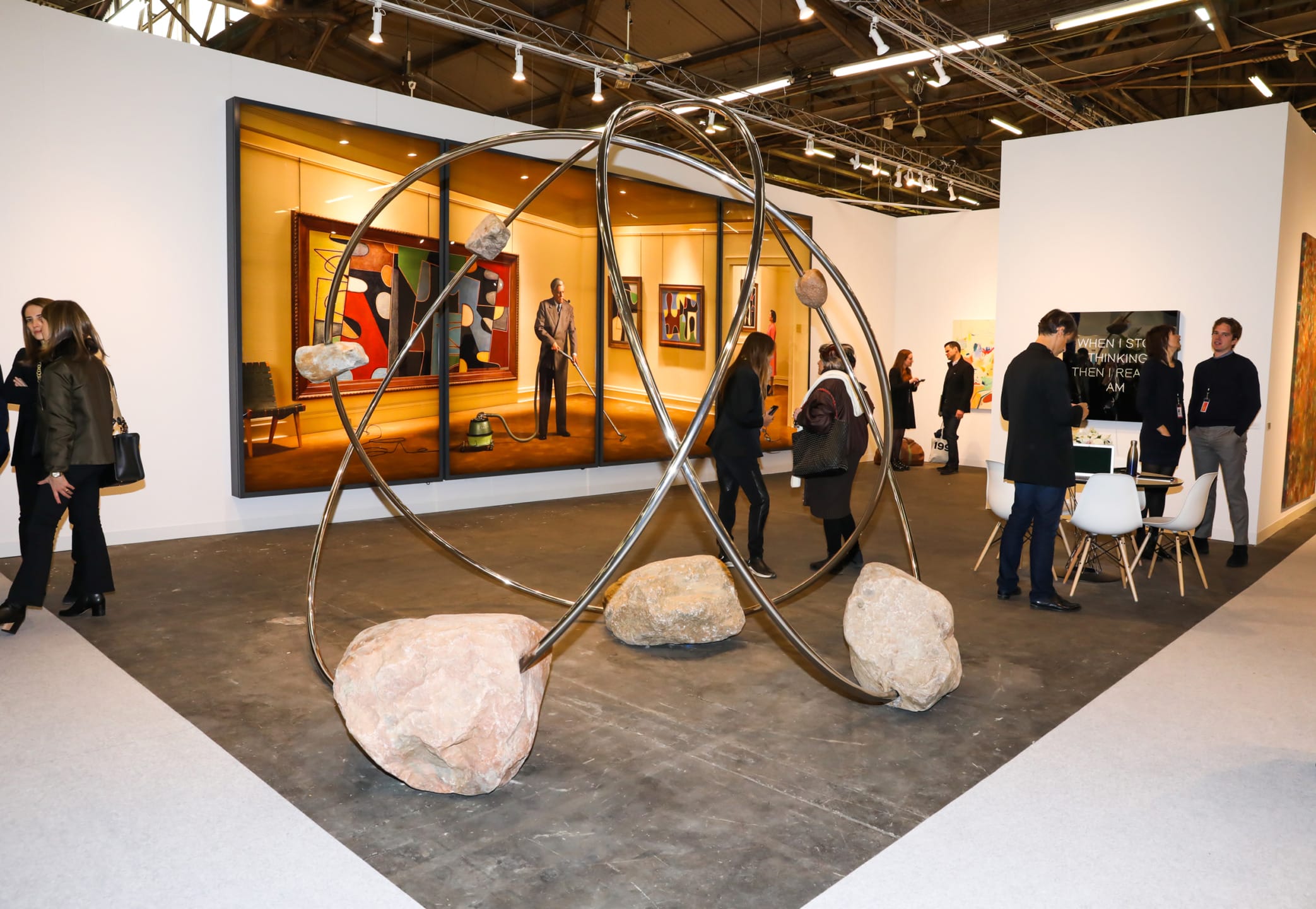 Visitors exploring a contemporary art exhibition with a prominent abstract sculpture and paintings in a modern gallery setting.